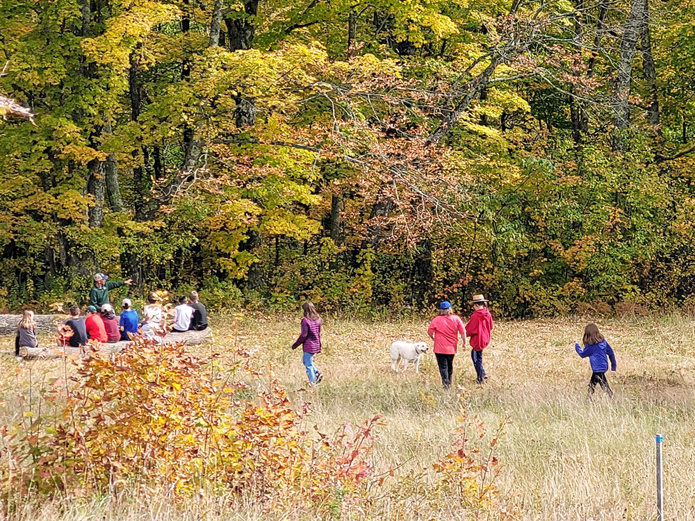 Group of middle school BFA students sitting as a group outdoors, with fall foliage in the background
