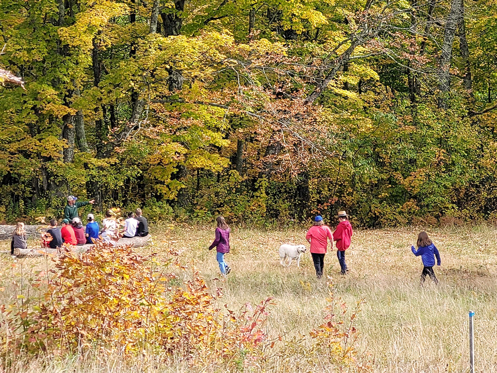 Group of middle school BFA students sitting as a group outdoors, with fall foliage in the background